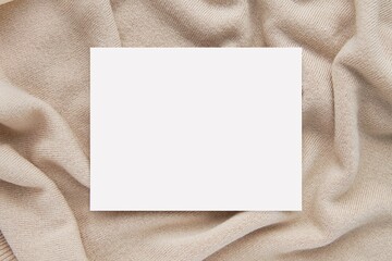 Small blank horizontal card on cream color knitted fabric or sweater, card mockup for washing, care instruction, apparel, fashion concept.