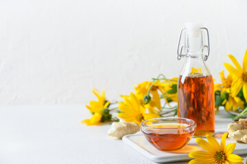 Jerusalem artichoke topinambour syrup in bottle, flowers and root on white background. Copy space.