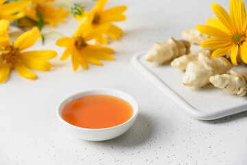 Jerusalem artichoke syrup in bowl, flowers and root on white background. Close up.