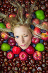 Fototapeta na wymiar Portrait, head of young beauty caucasian woman with blonde hair blinking from fruit and chestnut background. Health eating, diet, cosmetics concept