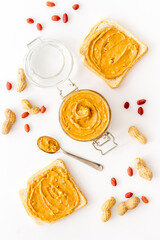 Glass jar of peanut butter with sandwiches and nuts on kitchen table