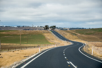 Winding open empty road surrounded by farms and fields in Australia. Road trip travel