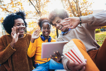 Mixed family having fun while picnicking in the park make video call.