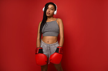 Exhausted young athlete woman boxer, sportswoman wearing wireless headphones, looks at camera...