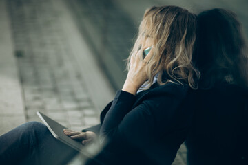 Business woman with smartphone in the hand and laptop on knees, bad news, depression, side view.