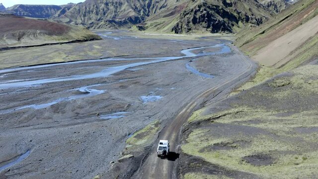 4x4 car driving on a grey gravel road between glacier river and mountain slopes covered by green moss in Iceland
