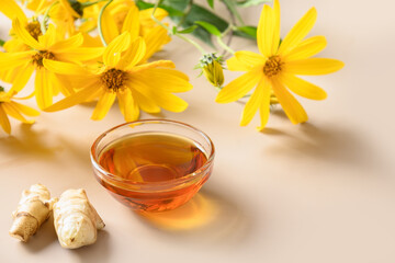 Jerusalem artichoke syrup in bowl, flowers and root on beige background. Close up. Copy space.