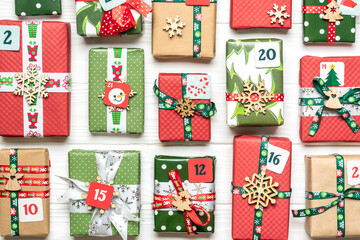 Handmade wrapped red, green gift boxes decorated with ribbons, snowflakes and numbers, Christmas decorations and decor on white table Xmas advent calendar concept Top view Flat lay Holiday card
