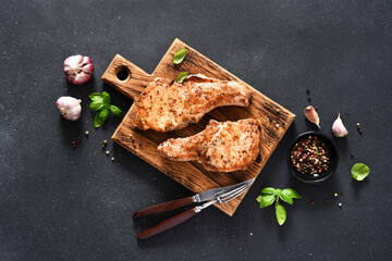 Two grilled pork steaks with garlic and basil on a wooden board on a black background with space...