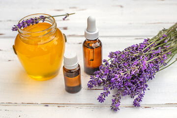 A jar of honey with lavender and essential oils on white wooden background. 