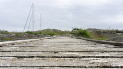 Fototapeta premium Empty wooden bridge leading toward small island with visible mast of sailboat in the background