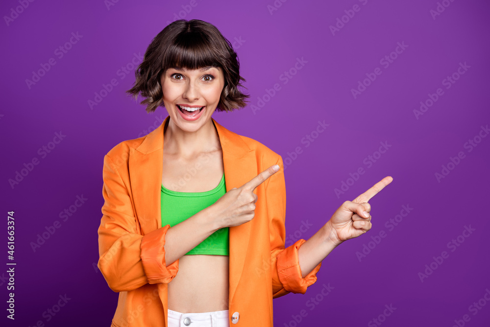 Poster Photo of impressed funny young woman dressed orange blazer pointing fingers empty space smiling isolated purple color background