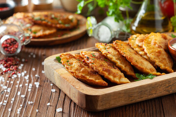 Traditional cheebureki, served on a wooden plate with sauce.