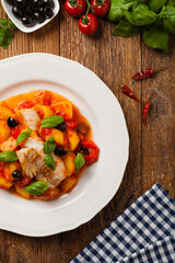 Traditionally prepared cod in Spanish. Served in tomato sauce with boiled potatoes, olivki and basil. Top view.