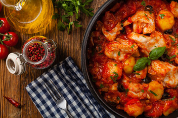 Traditionally prepared cod in Spanish. Served in tomato sauce with boiled potatoes, olivki and basil. Top view.