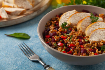 Trendy lunch with cereal, beetroot and chicken. Served in a bowl on a blue painted background. Front view.