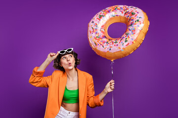 Photo of pretty shocked young lady wear orange jacket arm dark glasses looking holding donut...