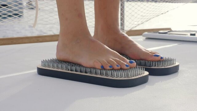Girl with a pedicure stands on sharp nails on the deck of a yacht against the background of the sea in the early morning at dawn. Female feet and Sadhu board close-up. Yoga. Meditation. Self-knowledge