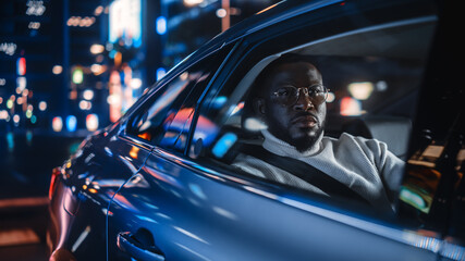 Stylish Black Man in Glasses is Commuting Home in a Backseat of a Taxi at Night. Handsome Male...
