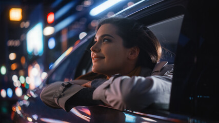 Fototapeta na wymiar Excited Young Female is Sitting on Backseat of a Car, Commuting Home at Night. Looking Out of the Window with Amazement of How Beautiful is the City Street with Working Neon Signs.