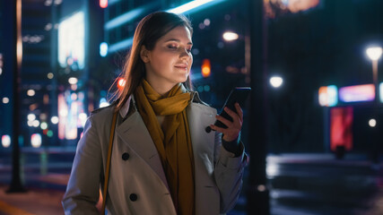 Portrait of a Beautiful Woman in Trench Coat Walking in a Modern City Street with Neon Lights at...