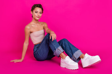 Full length photo of attractive cool young woman sit floor wear jeans white platform shoes isolated on magenta color background