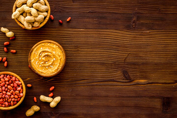 Creamy peanut butter and nuts in wooden bowls, top view