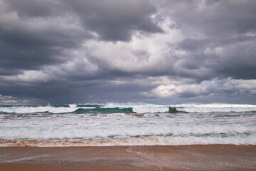 Storm clouds over rough ocean seas with waves breaking onto a sandy beach, beautiful coastal location in Victoria, Australia.
