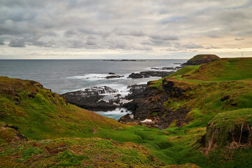 A scenic view overlooking green grassy hills with beautiful volcanic, rocky coastline in the...