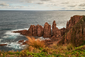 A scenic view overlooking waves breaking against red pillars of rock with the vast ocean on the...