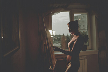 A beautiful girl is dressed in a bodysuit. The girl the artist draws on the easel.