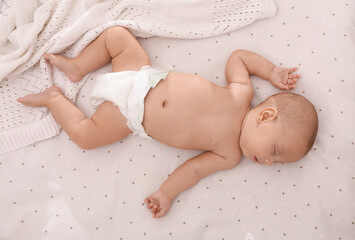 Cute little baby in diaper sleeping on bed, top view