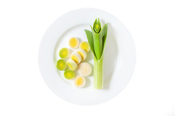 Sliced fresh raw leek wedges and a long stalk of leeks on a white round plate. Isolate on white background