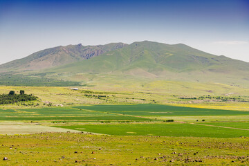 View of the ancient extinct volcano Mount Arayi Lerr and the fertile valley at its foot with agricultural lands sown in early spring in Armenia