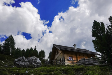 Fototapeta na wymiar wooden alpine hut with a fence on a hill with amazing clouds on the sky