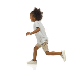 Happy small black boy in shorts and shirt is running. Side view. Full length, isolated.
