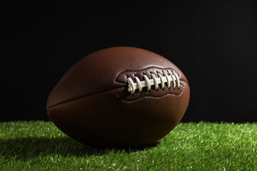 American football ball on green grass against black background