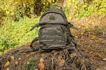 one big green tactical backpack stand on dry gray vegetation with leaves in nature
