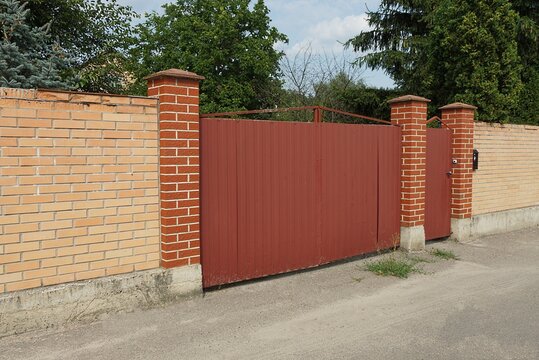 red metal gate and closed door on the wall of the brown brick fence on the street