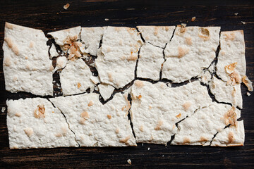 Dry flat bread broken in pieces and divided, with crumbs,  on dark wooden background
