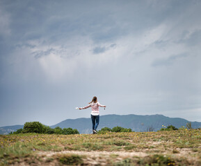 Fototapeta premium Smiling and cheerful young girl who feels free in the mountains on a cloudy day with dramatic sky, she wears a mask and the car keys in her hand