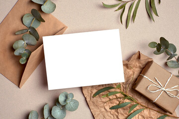 Greeting card mockup, flat lay with gift box, envelope and natural eucalyptus twigs on paper background.