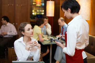 Waitress taking order from business woman working in coffee shop