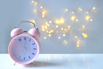 Fototapeta na wymiar pink lady's alarm clock in retro style on light background with bokeh, 7 a.m., selective focus, copy space for designer, concept of routine of female life, device to get up on time, good morning