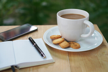 Coffee cup with butter cookies, Blank opened notebook with pen and smart phone on wooden table, Coffee break time and writing idea concept, Natural background