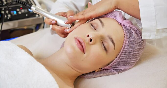 Beautiful woman receiving facial microcurrent treatment at spa salon. Beautician using electrical impulses for facial procedures. Woman in spa salon. Woman in a spa salon on cosmetic procedures.