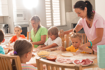 Two middle-aged women with little children are making pizza