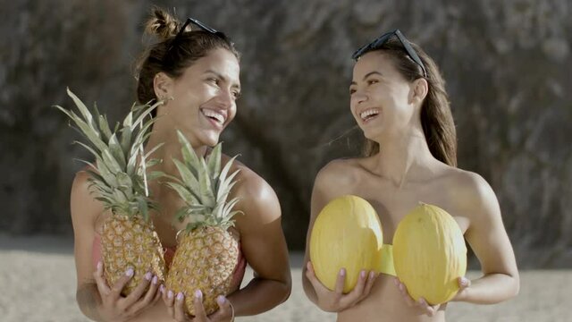 Front view of smiling women with pineapples and melons on beach. Handheld shot of female friends in bikini having fun together during vacation at sea. Joy, resort concept