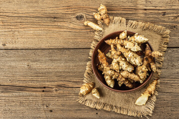 Raw Jerusalem artichoke in a bowl on wooden boards background