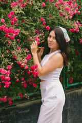 young pretty smiling woman near blooming red roses bush